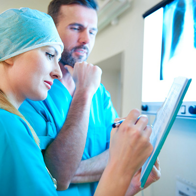 Une femme médecin et un homme médecin en blouse bleues regardent ensemble des résultats de radiographie